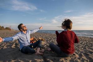 jeune couple assis sur la plage à côté d'un feu de camp buvant de la bière photo