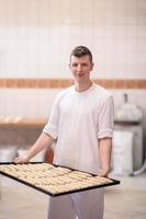 un jeune boulanger tenant un produit cru de pâte blanche photo