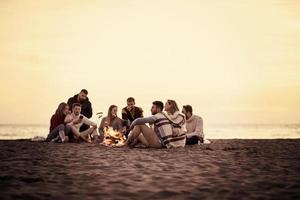 groupe de jeunes amis assis près du feu à la plage photo