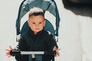 doux petit garçon dans un vélo poussette à l'extérieur. petit enfant dans un landau. enfant en bas âge dans une poussette. promenades printanières avec les enfants. photo