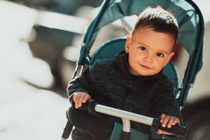 doux petit garçon dans un vélo poussette à l'extérieur. petit enfant dans un landau. enfant en bas âge dans une poussette. promenades printanières avec les enfants. photo