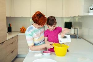 une petite fille amusante jouant avec de la pâte sur ses mains apprenant à pétrir aide une maman adulte dans la cuisine, une petite fille mignonne et heureuse et une maman parent s'amusent à cuisiner des biscuits. photo