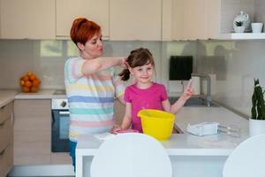 une petite fille amusante jouant avec de la pâte sur ses mains apprenant à pétrir aide une maman adulte dans la cuisine, une petite fille mignonne et heureuse et une maman parent s'amusent à cuisiner des biscuits. photo