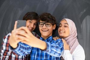 groupe d'adolescents arabes prenant une photo de selfie sur un téléphone intelligent avec un tableau noir en arrière-plan. mise au point sélective