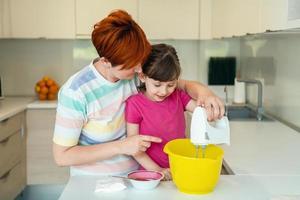 une petite fille amusante jouant avec de la pâte sur ses mains apprenant à pétrir aide une maman adulte dans la cuisine, une petite fille mignonne et heureuse et une maman parent s'amusent à cuisiner des biscuits. photo