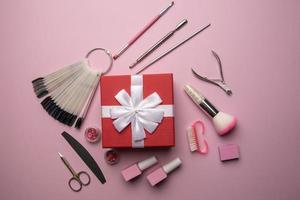 ensemble d'outils et d'accessoires de manucure avec boîte-cadeau rouge sur fond rose. manucure matérielle, mise à plat. photo