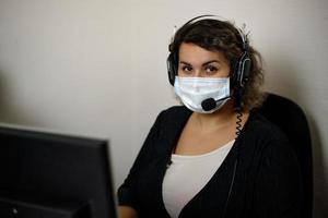 un agent du centre d'appels travaillant sur la hotline d'assistance au bureau, portant un masque et des gants. l'opérateur du centre d'appels parle au client. photo