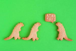 biscuits faits maison en forme de dinosaures avec inscription - rester en sécurité - sur fond vert, vue de dessus. sablé sucré avec glaçage blanc. concept de distanciation sociale. photo