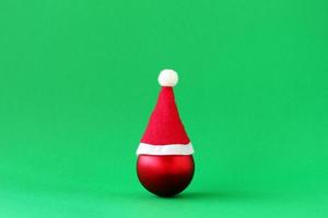 boule de noël rouge avec chapeau rouge du père noël sur fond vert avec espace de copie. concept minimal de noël et du nouvel an. photo