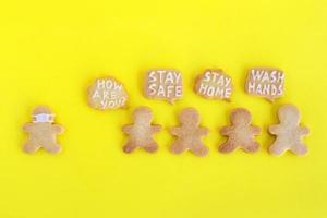 biscuits sablés faits maison avec glaçage blanc sur fond jaune, vue de dessus. foule de personnes et un homme en masque facial et avec des nuages de légende avec des inscriptions sur le thème de la distanciation sociale. photo