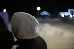 capuche blanche et veste noire. homme dans la rue la nuit. lumière froide. photo