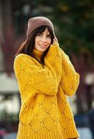 belle brune européenne vêtue d'un pull en laine jaune et d'un chapeau à l'extérieur. la belle fille qui porte des vêtements d'automne épais et élégants par temps frais. photo