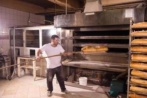 Ouvrier de boulangerie sortant des pains fraîchement cuits photo