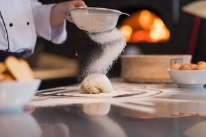 chef saupoudrant de farine sur la pâte à pizza fraîche photo