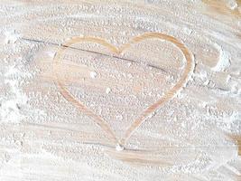 coeur dessiné par le doigt avec de la farine sur une table en bois photo
