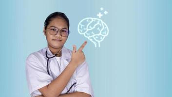 portrait d'une femme médecin portant des lunettes debout avec les bras croisés sur un fond vert clair. main pointant vers l'icône du cerveau. concepts de médecine, de traitement des maladies et de santé. photo