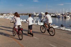 famille heureuse profitant d'une belle matinée au bord de la mer ensemble, parents faisant du vélo et leur fils faisant du scooter électrique. mise au point sélective photo