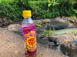 blitar, indonésie - 2 octobre 2022 boisson au thé aux fruits rechargeable de marque sosro avec un goût de cassis désaltérant lorsqu'elle est sortie dans la nature. objets avec un fond de rivière nuageux photo