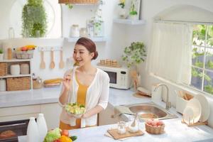 portrait en gros plan d'une jolie fille mangeant de la salade dans la cuisine photo