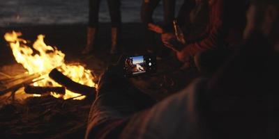 couple prenant des photos à côté d'un feu de camp sur la plage