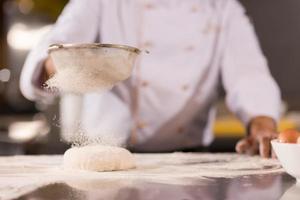 chef saupoudrant de farine sur la pâte à pizza fraîche photo