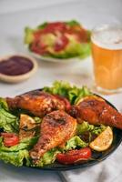 cuisses de poulet grillées rôties sur le gril sur une assiette sombre avec sauce tomate dans un bol et feuilles de laitue, chope de bière en verre photo