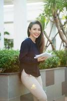 portrait d'une étudiante souriante lisant un livre tout en se tenant à l'extérieur sur la terrasse du café du campus en journée ensoleillée. concept d'éducation, de style de vie et de personnes. photo