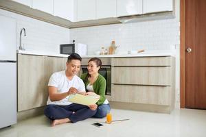 beau jeune couple amoureux assis sur le sol de la cuisine, lisant le plan photo