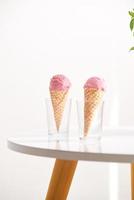 cornet gaufré rempli de crème glacée à la framboise fraîche dans une tasse en verre avec des framboises fraîches assises sur la table photo