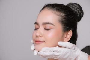 portrait d'une jeune femme asiatique recevant un traitement médical de beauté isolé sur fond gris photo