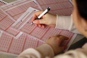 remplir un ticket de loterie. une jeune femme joue au loto et rêve de gagner le gros lot. numéro de marquage de la main féminine sur le billet de loterie rouge photo