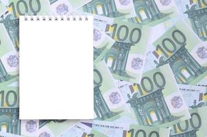 cahier blanc avec des pages propres se trouvant sur un ensemble de coupures monétaires vertes de 100 euros. beaucoup d'argent forme un tas infini photo