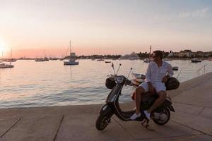 un homme d'affaires senior moderne en vêtements décontractés assis sur un scooter au bord de la mer et profite du lever du soleil. mise au point sélective photo