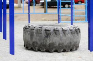 un grand pneu noir contre un terrain de sport de rue pour l'entraînement d'athlétisme et de crossfit. équipement de gym athlétique en plein air. photo macro avec mise au point sélective et arrière-plan flou