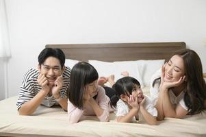 portrait de parents asiatiques avec deux petites filles sur le lit dans la chambre, concept de famille heureuse photo