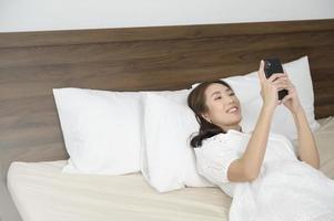 jeune femme asiatique utilisant un smartphone avant le coucher, concept de style de vie heureux photo