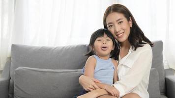portrait d'une maman asiatique et d'une petite fille souriante sur un canapé à la maison photo