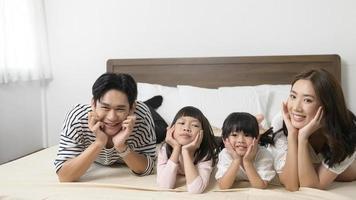 portrait de parents asiatiques avec deux petites filles sur le lit dans la chambre, concept de famille heureuse photo