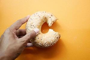 tenant un pain bagel frais sur fond orange photo