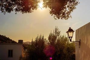 vue sur le soleil couchant du côté de la maison avec une lanterne entourée de feuillage d'arbre photo