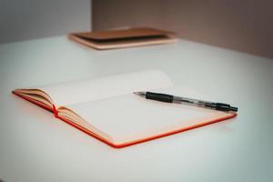 photo sous un petit angle d'un stylo noir posé sur un journal ouvert rouge sur la table