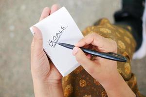 main de femmes écrivant des objectifs du nouvel an sur le bloc-notes photo