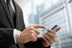 gros plan de la main d'un homme d'affaires à l'aide d'un téléphone intelligent mobile de texte tenant un appareil et d'un écran tactile. ou contacter le client. debout sur fond de lumière dans le bâtiment. photo