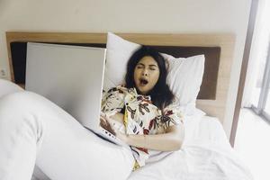 une jeune femme endormie bâillant en travaillant depuis le lit. photo