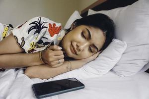 triste jeune femme fronçant les sourcils du lit attendant un appel tout en tenant le smartphone. photo
