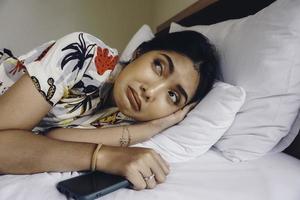 triste jeune femme fronçant les sourcils du lit attendant un appel tout en tenant le smartphone. photo