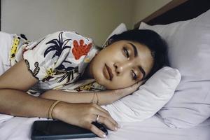 une jeune femme asiatique sur le lit a sommeil, elle est allongée sur le côté et bâille photo