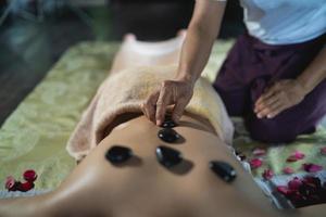 massage et spa traitement relaxant du syndrome de bureau en utilisant le style de massage thaï traditionnel aux pierres chaudes. masseuse féminine asiatique faisant des massages pour traiter les maux de dos, les douleurs au bras, le stress pour les femmes fatiguées du travail. photo