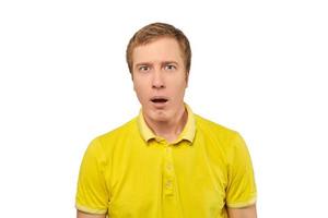 jeune homme perplexe avec drôle de visage et bouche ouverte en t-shirt polo jaune, fond blanc isolé photo