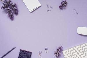 l'espace de travail d'un blogueur ou d'un pigiste est à plat avec un clavier, des cahiers et des branches lilas, des articles de papeterie sur fond lilas avec un espace de copie photo